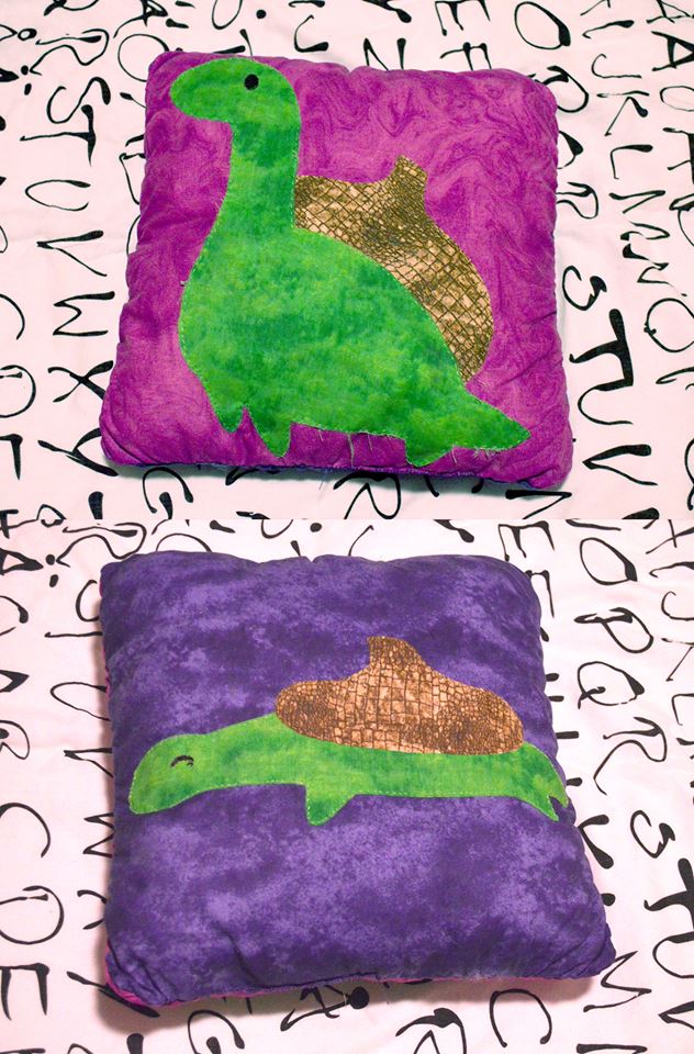 a pillow displaying a tiny dinosaur with the top of a nut on his back