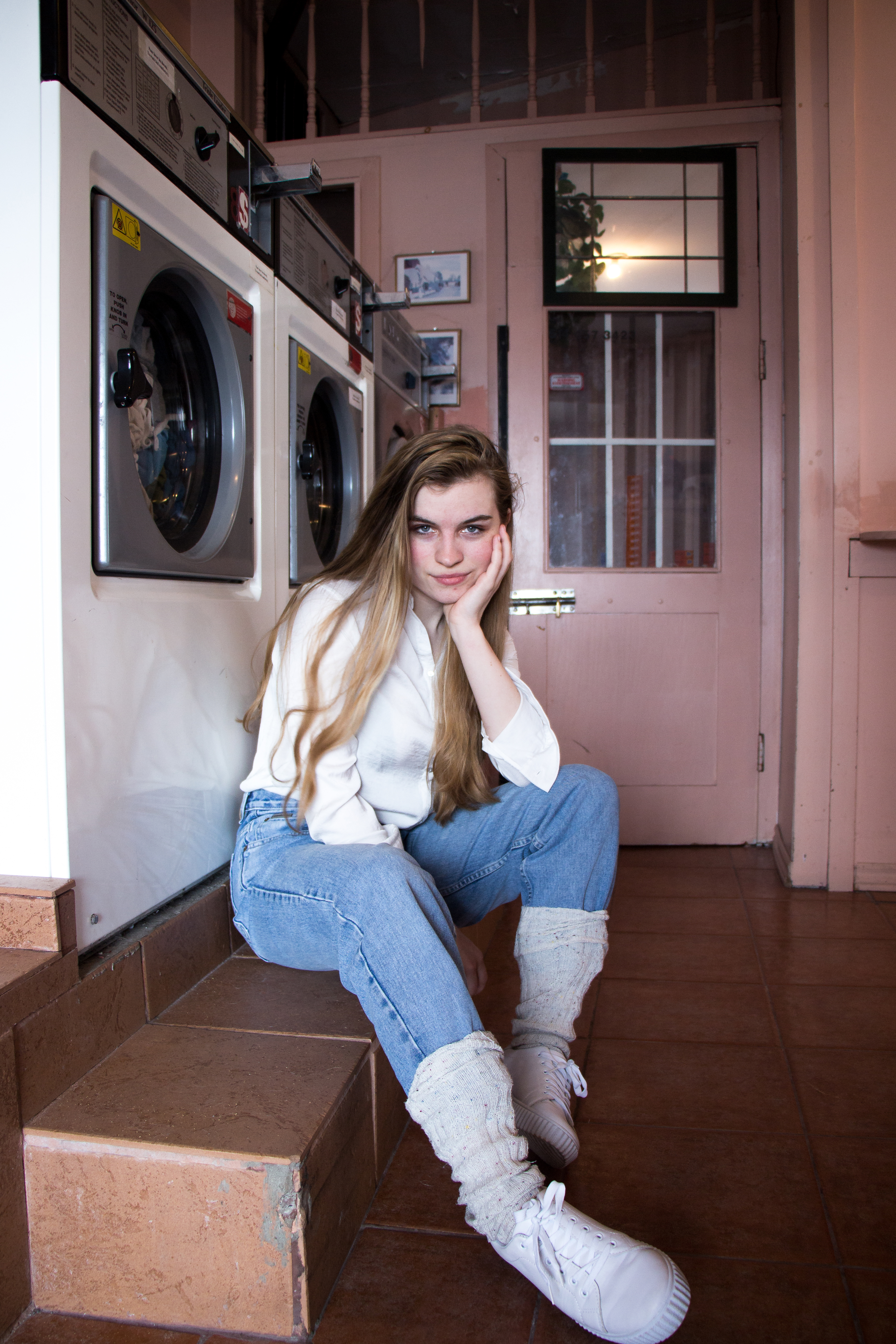 girl sitting waiting for her laundry in a pink laundromat