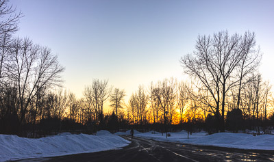 A picture of the sunset with trees and snow on the ground