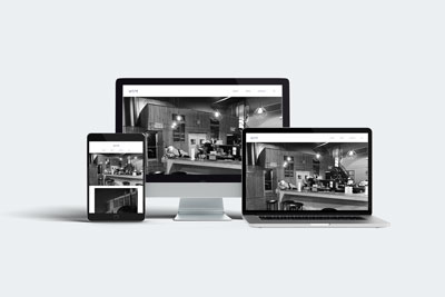 Mac screen mock-up in the back with a cafe website displaying a large hero image in black and white of Café Ole. Laptop in front right with same website, and tablet on the left with tablet version of website.