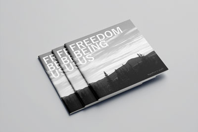 Three Freedom Being Us look books laid staggered on top of each other. On the cover is a black and white shot of mountain range