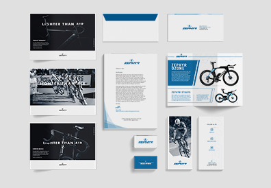 Zephyr Performance mockups arranged over grey background. Three posters on the far left containing cycling racing and bicycles, letterhead in the center with business cards underneath. To the right lie 3-fold brochures with envelopes at the top.